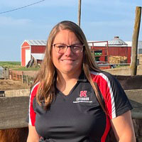 A woman with long blond hair and glasses standing in front of a red barn