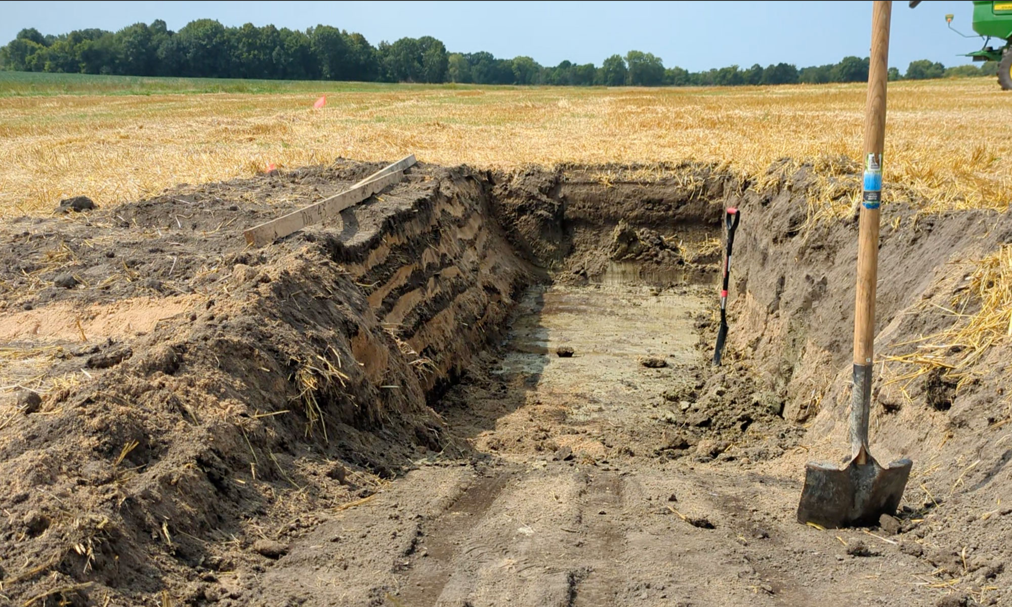 A large pit dug in the middle of a field showing the soil layers.